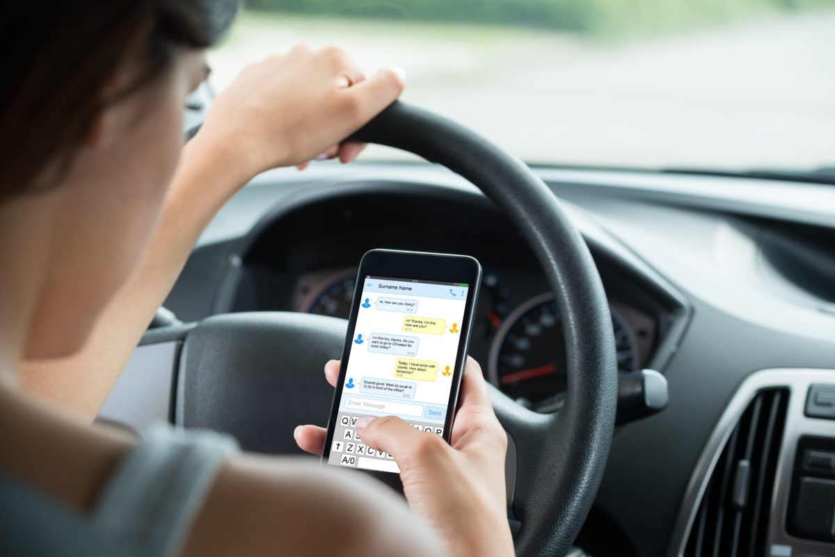 Donna al volante guida mentre si distrae a guardare il cellulare.jpg