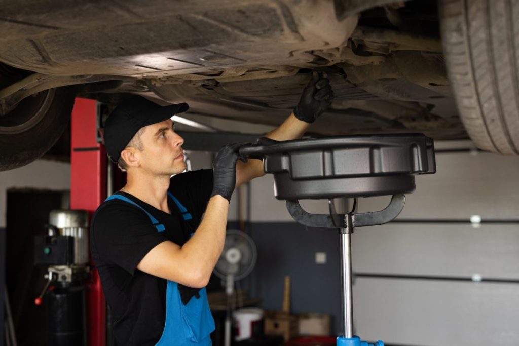 Meccanico effettua il Cambio olio motore a un auto in officina.jpg
