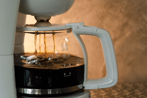 photograph of a dripping half full white coffee pot on brown background m.png