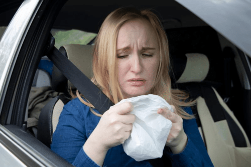 person in a car holding a white plastic bag looking nauseous m.png