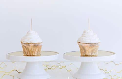 photograph of two identical cupcakes with white icing and a toothpick sticking out side by side on identical white stands m.jpg