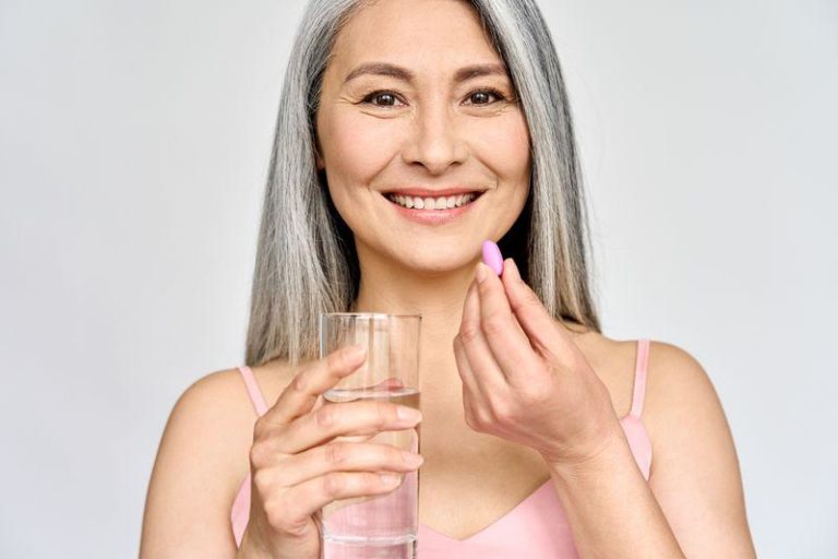 grey haired woman in pink tank top taking a pink pill holding a glass of water m.jpg