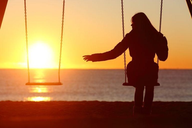 person silhouetted sitting on swing in the sunset reaching out to an empty swing next to them m.jpg