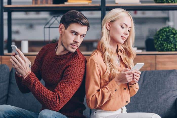 brown haired man in red sweater looking suspiciously at the phone of a blonde woman in a brown shirt m.jpg