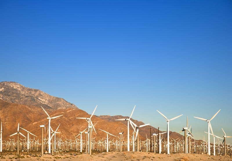 row of wind turbines under a blue sky orange brown mountain in the background m.jpg
