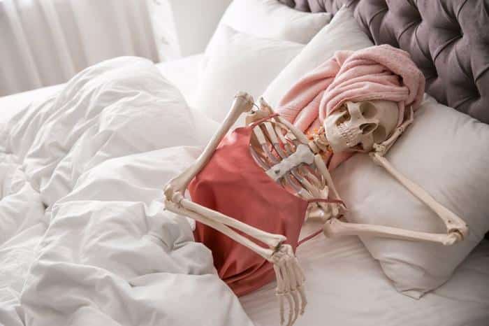 skeleton in a pink silk tank top and head towel lounging in bed skull resting on its hand m.jpg