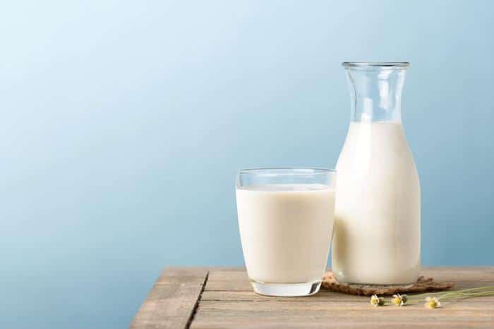 a carafe and a glass of milk on a wooden table in front of a blue wall m.jpg