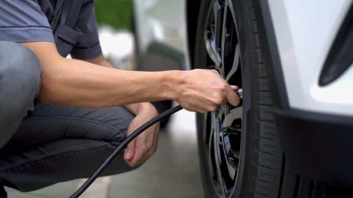 person in jeans and blue t shirt crouching down holding a black rubber hose attached to a car tire m.jpg