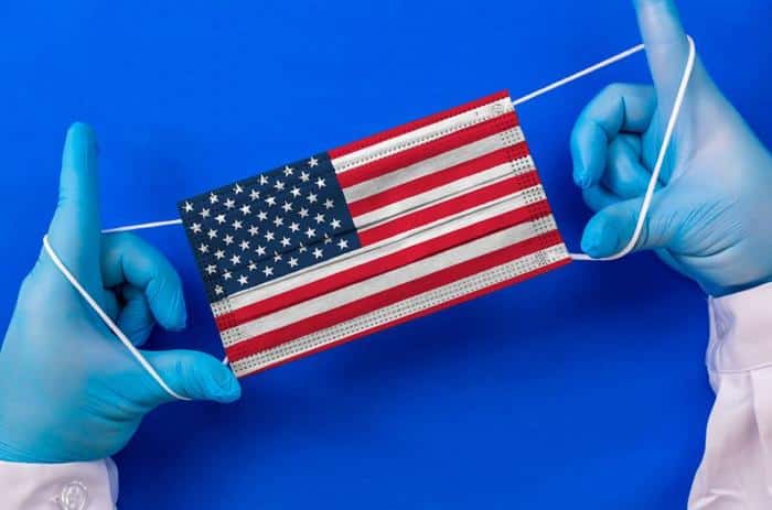 blue gloved hands stretching out a surgical mask printed with the usa flag m.jpg