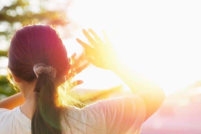 Caldo estremo in Europa: impatto del riscaldamento globale 1 person with dark hair in a ponytail holding their hands up to shield themselves from the bright sun m.jpg