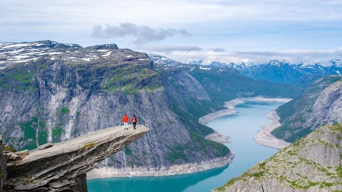 two hikers stand on the edge of trolltunga norway a massive cliff overlooking a stunning fjord in norway m.jpg
