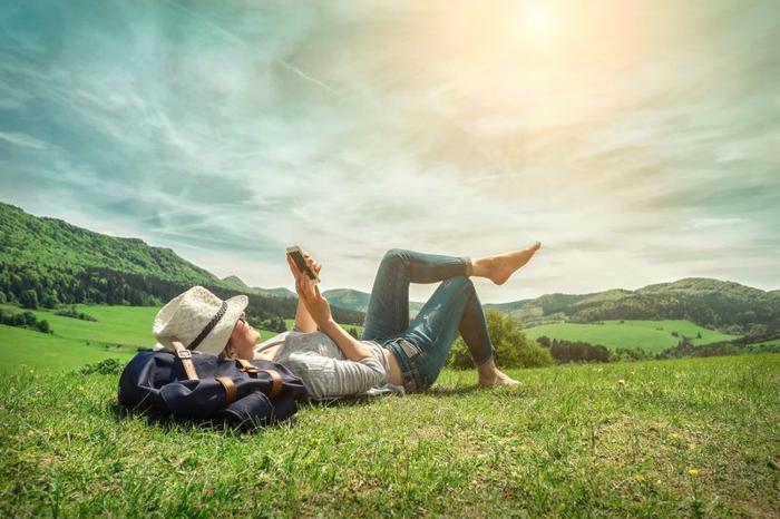 woman holding a phone lounging on sunny grassy hill next to a backpack m.jpg